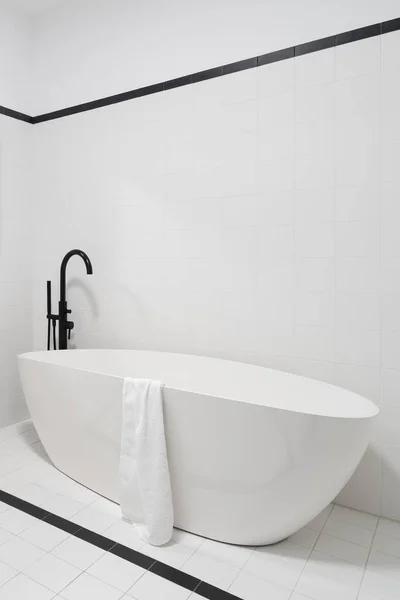 在黑白瓷砖的简约浴室里配备黑色水龙头的精致独立浴缸 — 图库照片