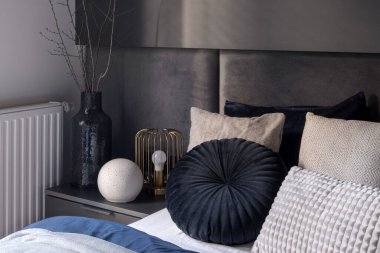 Yatağın yanında vazo ve lambayla süslenmiş, güzel yastıklar ve çarşaflarla süslenmiş.