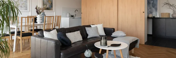 Panorama of black corner sofa and two coffee table in modern living room open to dining area and kitchen