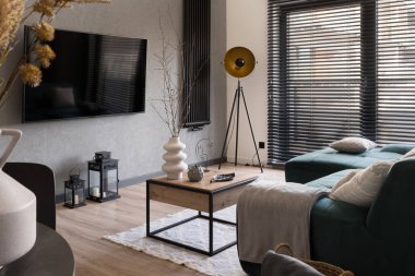 Büyük televizyonlu modern oturma odası, şık mobilyalar ve siyah perdeli büyük bir pencere.
