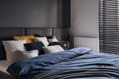 Çift kişilik yatağı, koyu gri duvarları, şık çarşafları ve yastıkları olan rahat ve zarif bir yatak odası.