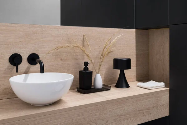 Stylish, small oval bathroom washbasin with black tap on wooden shelf with elegant decorations