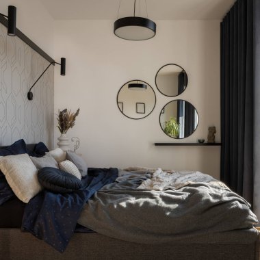 Cozy and stylish bedroom with big, comfortable bed with bedclothes, many decorations and round mirrors
