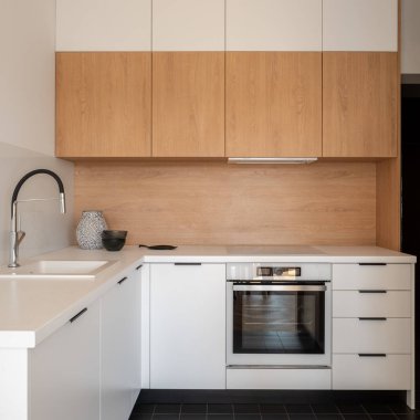 Beyaz ve ahşap dolapları, tezgahları, çekmeceleri, fırını ve lavabosu olan küçük ve basit bir mutfak.