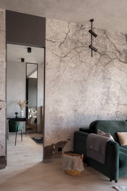 Gri duvarları ve beton tavanı olan şık bir oturma odası. Kapıları açık, rahat yeşil bir kanepe. Çalışma odası, küçük masa, yeşil sandalye ve dekorasyonlar.