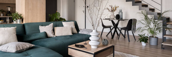 Panorama of open living room with cozy green sofa and dining table under stairs