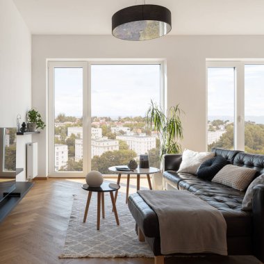 Modern and bright living room with big windows, wooden floor and stylish sofa with coffee table
