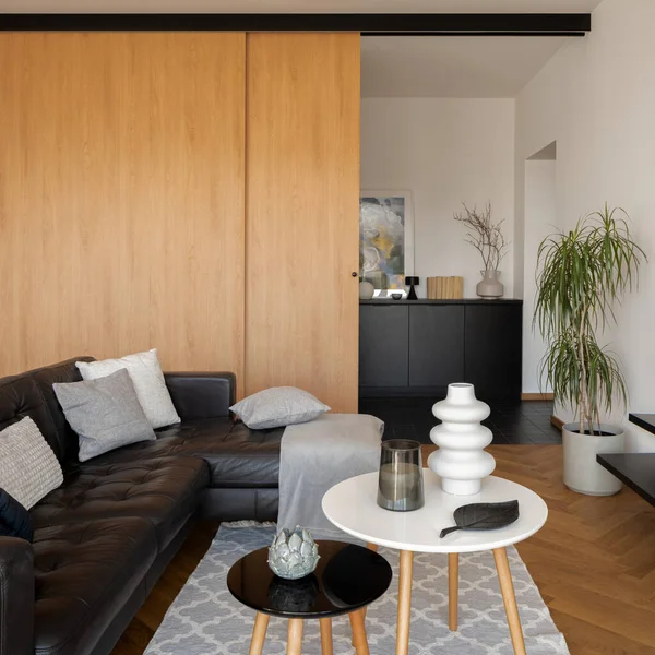 Modern living room with leather, black corner sofa, simple coffee tables with decorations and wooden, sliding doors