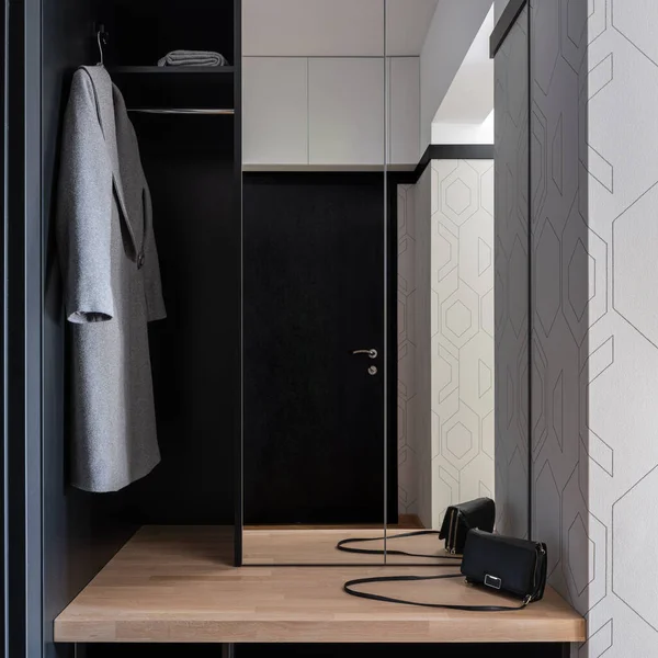 Elegant apartment corridor with black main doors, wardrobe with big mirror and wooden shelf