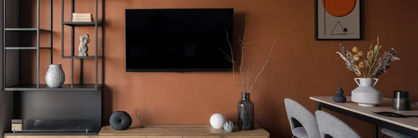 Panorama of television screen on orange wall in stylish room with dining table and decorations