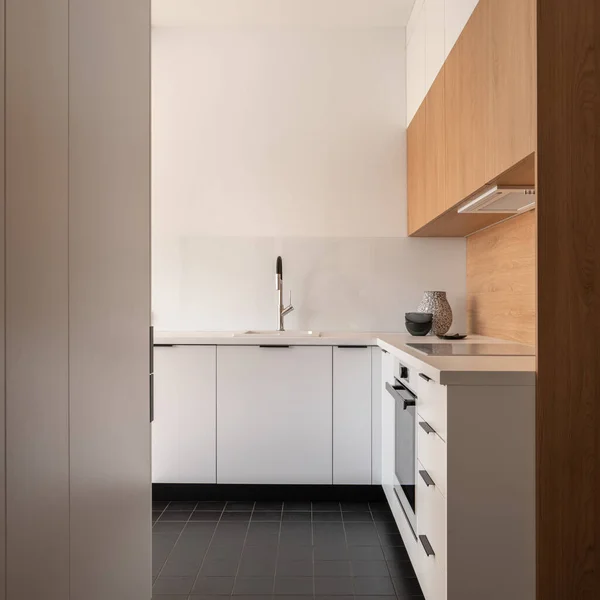 Simple and minimalist kitchen interior with dark tiled floor, white cupboards and drawers and wooden wall