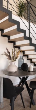 Vertical panorama of small, round dining table with decorations under wooden stairs