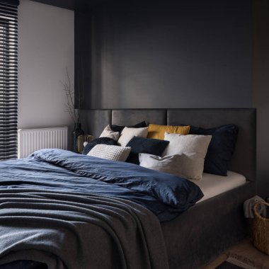 Big and cozy bed in modern and dark bedroom with gray wall and headboard