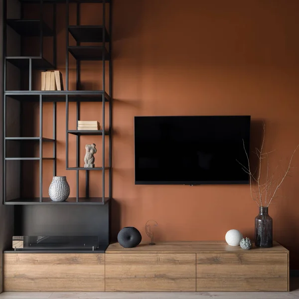 Close-up on television screen on modern orange wall in room with stylish black shelves and wooden cabinet