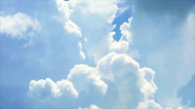 Büyük bir yığın parlak beyaz bulut yazın mavi gökyüzü arka planında hareket ediyor.