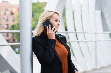 Woman in formal clothes leaning on a post while talking to the mobile phone in the street