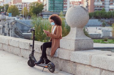 Young woman with protective mask downloads the application to use the electric scooter in the city streets sustainable lifestyle