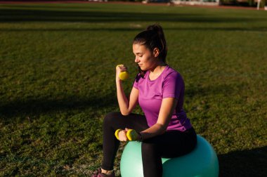 Fitball üzerinde oturan ve dumbbells ile egzersizleri yapıyor kadın