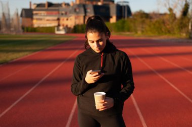 young athlete looks at the mobile while having a coffee on the running track