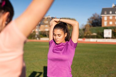 two young women doing stretching on the grass of a running track before playing sports