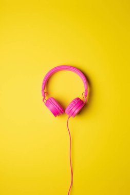 pink wired headphones centered on a flat yellow background, vertical image