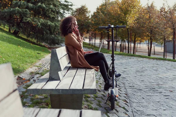 Жінка Сидить Лавці Парку Розмовляє Телефону Має Ноутбук Електричний Скутер — стокове фото