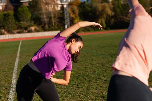 Dos Mujeres Jóvenes Haciendo Estiramiento Hierba Una Pista Atletismo Antes — Foto de Stock