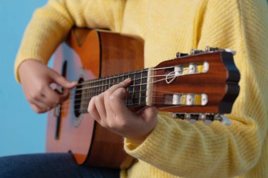 Klasik gitar çalan, mavi arka planlı bir kadının ellerinin stüdyo portresi.