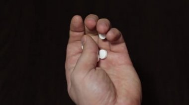 Elinde beyaz haplar tutan bir adama yaklaş. Adam ilaç almadan önce endişeleniyor.