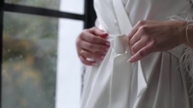 A girl near the window in a dressing gown, holding a belt with her hand