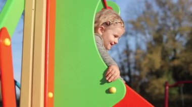 Çocuk bahçede oyun oynuyor, kaydırağa biniyor, kızın keyfi yerinde, neşeli.