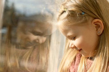 Evdeki pencerenin yanında küçük bir çocuk. Çocuk güvende, yüzünde güneş ışığı var.