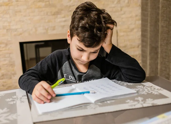 Cheerful and funny schoolboy solves his homework emotionally. Thinks about how to solve math examples by holding his head. — Stock Photo, Image