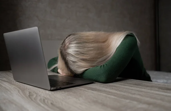 Een blond meisje werkt thuis op een laptop, ze is erg moe en legt haar hoofd op tafel. Afstandsonderwijs. Freelance. Uitputting van de werkgelegenheid — Stockfoto