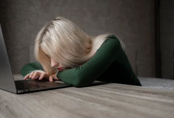 Een blond meisje werkt thuis op een laptop, ze is erg moe en legt haar hoofd op tafel. Afstandsonderwijs. Freelance. Uitputting van de werkgelegenheid — Stockfoto