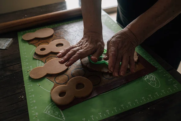 Grandmother makes gingerbread cookies with her hands and cuts out figure eights for March 8. Baking equipment. Home cooking handmade. Senior woman — Stock Photo, Image