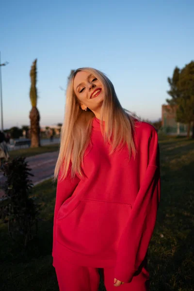 Pembe yünlü eşofmanlı mutlu, gülümseyen sarışın kız dışarıda iyi vakit geçiriyor. Aktif eğlencenin keyfi.