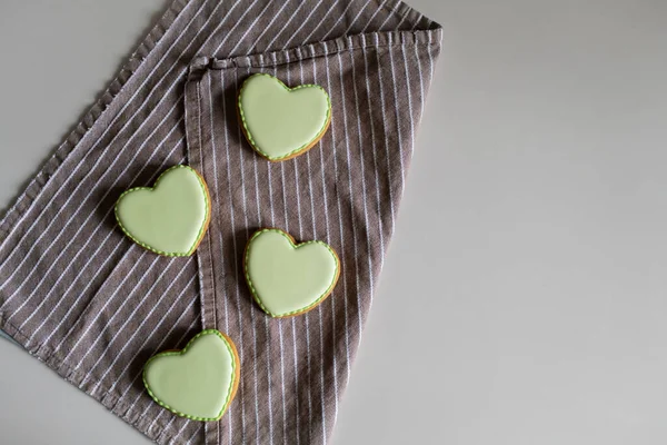Pão de gengibre na forma de corações na cobertura verde em uma chapa branca com uma toalha. Local para texto, fundo ou cartão postal. — Fotografia de Stock