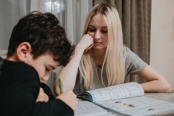Mutlu anne ve oğul ödev yapıyor. Kız kardeş, erkek kardeşin matematiği çözmesine yardım eder. Evde eğitim.
