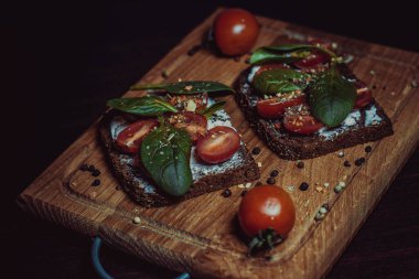 Krem peynirli sandviç, kiraz domatesleri, ıspanak ve baharatlar tahtada. Ev ve restoran mutfağı. Lezzetli sağlıklı sebze yemeği..