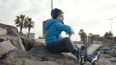 Okul çağındaki bir çocuk taşların üzerine oturur ve denize ya da okyanusa çakıl taşları atar. Sonbahar ya da ilkbahar. Sahil. Dinlenme ve faaliyet.