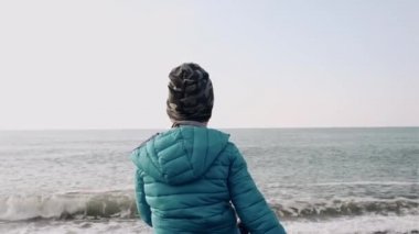 Okul çağındaki bir çocuk taşların üzerine oturur ve denize ya da okyanusa çakıl taşları atar. Sonbahar ya da ilkbahar. Sahil. Dinlenme ve faaliyet.