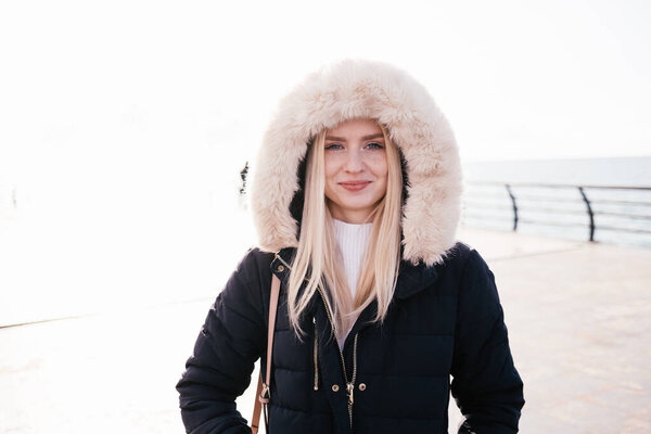 Happy smiling blonde girl in a fluffy hood on a white background. Portrait.