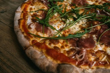 Prosciutto ve ahşap masada salamlı leziz sıcak et pizzası..