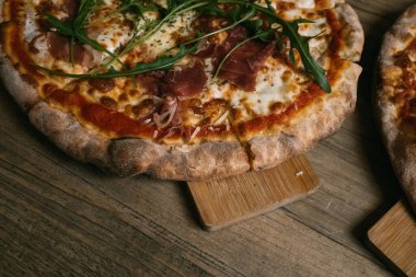 Prosciutto ve ahşap masada salamlı leziz sıcak et pizzası..