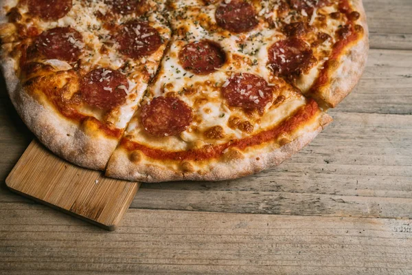 Prosciutto ve ahşap masada salamlı leziz sıcak et pizzası..