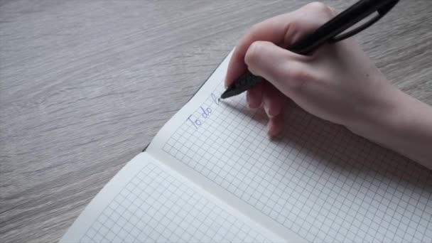 一个女人的手把她要做的事的清单用笔写在笔记本上。主办单位. — 图库视频影像
