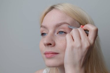 Çilli güzel sarışın bir kız cımbızla kaşlarını yoluyor. Doğal güzellik..