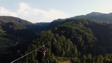 Bir kız uzanmış kollarıyla ulusal parktaki bir halatla tepeden tepeye iniyor.