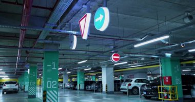 Alışveriş merkezinde park etmiş araçlar ve trafik işaretleri olan yeraltı otoparkı.